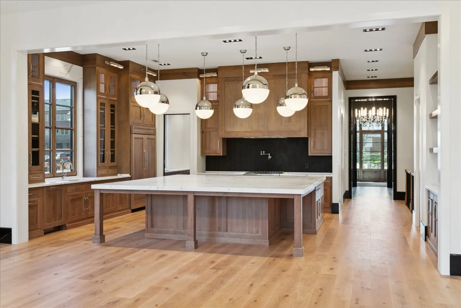 Finished BAC kitchen with central island, warm wood cabinetry, pendant lighting, and black backsplash